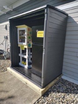 Mini food pantry box and a black refrigerator next to the community center.